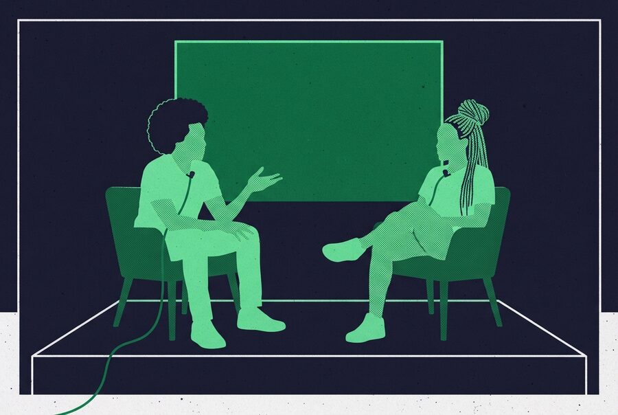 two people in low chairs mid-conversation, clip mics on, a blank screen behind