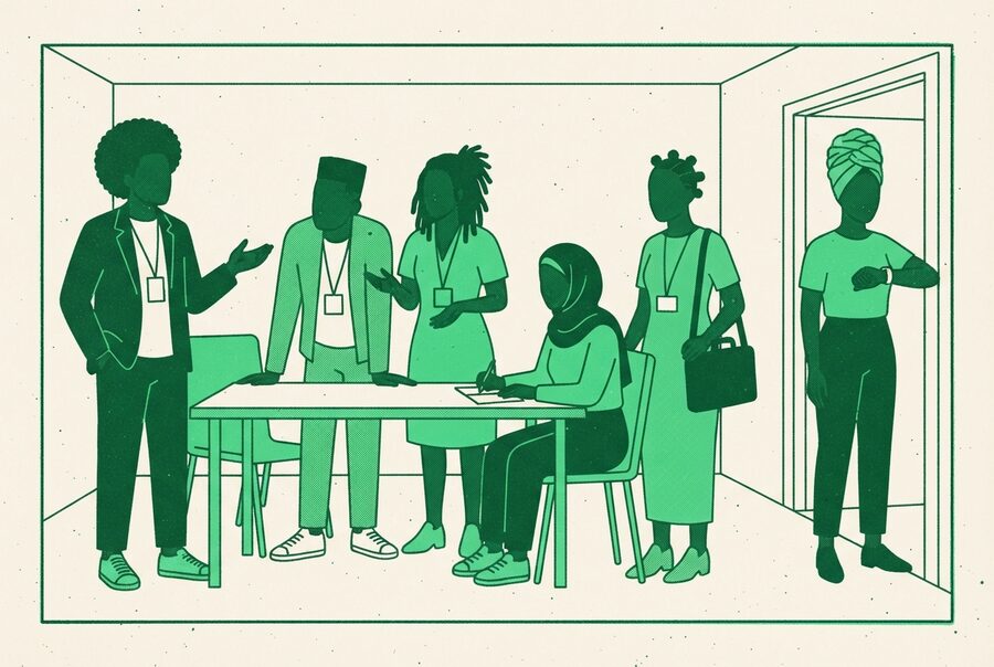 a room mid-session, lanyards on, one person talking across the table